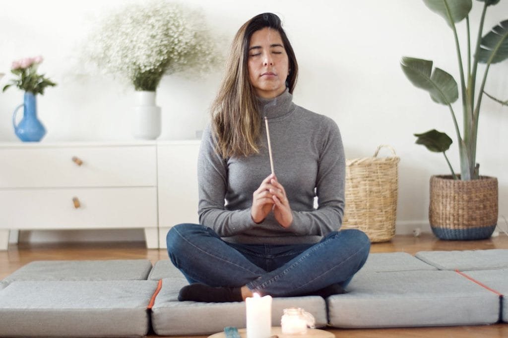 A woman practicing mindfulness meditation indoors, holding incense.