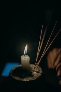 A close-up of a lit candle and incense sticks in a calming indoor setting.